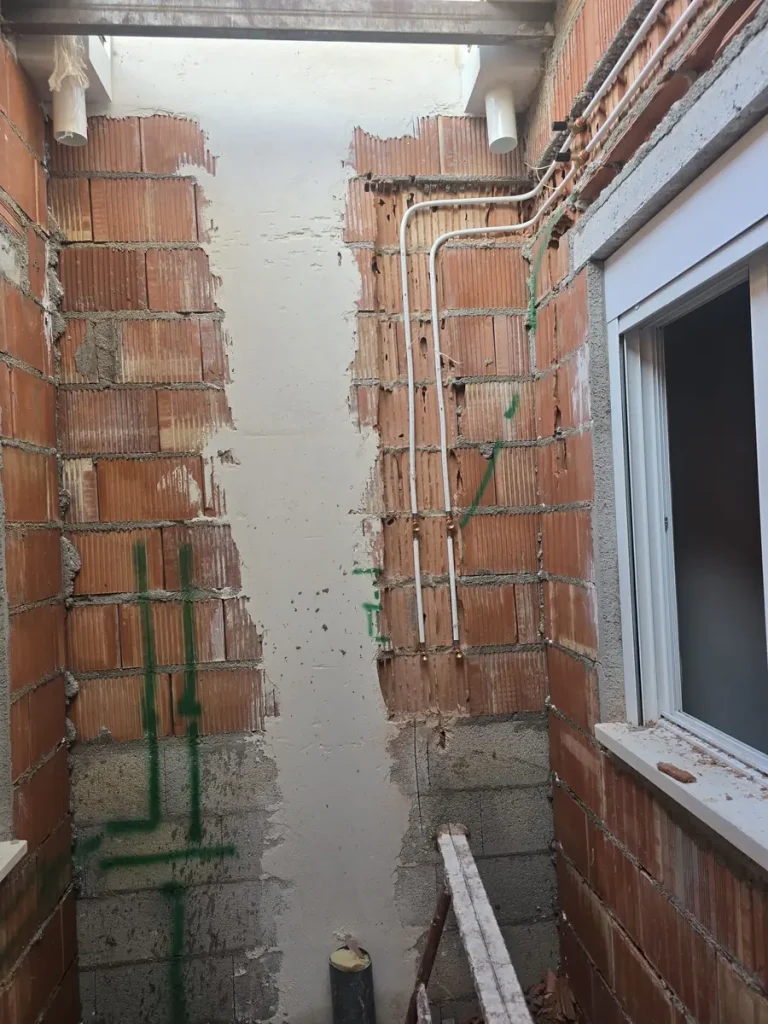 Rozas abiertas en el muro con la tubería de agua fría y caliente ya pasada, en una obra de Murcia